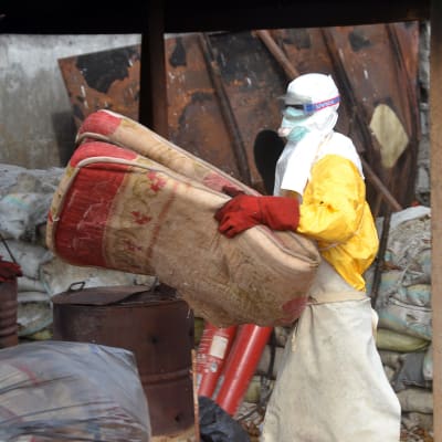 En hjälparbetare i skyddsutrustning flyttar en madrass i Guinea i december ifjol.
