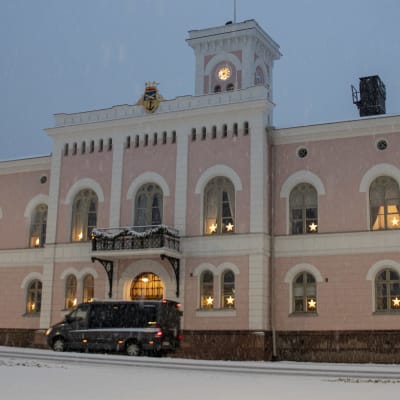 En taxi kör förbi en rosa rådhusbyggnad, där fönstren är dekorerade med julbelysning.