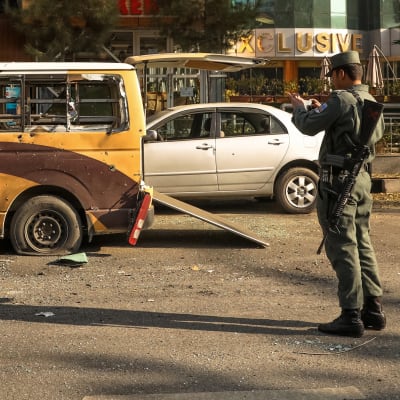 En soldat står bredvid en minibuss som har flera hål av splitter.
