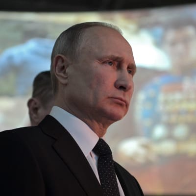 Putin vakavailmeisenä, taustalla valokuva, jossa univormupukuinen mies. 