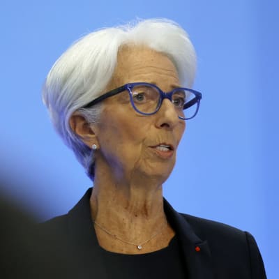 Christine Lagarde klädd i svart talar vid ett podium med texten European Central Bank - Eurosystem. I förgrunden syns huvuden av personer i publiken.