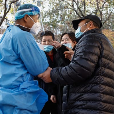 Ihmiset väittelevät terveydenhuoltohenkilön kanssa koronatestipaikalla Kiinassa.