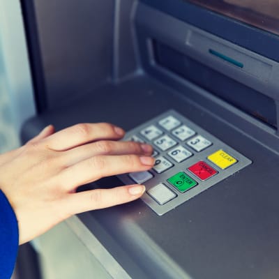 Hand knäpper in pinkod på bankautomat