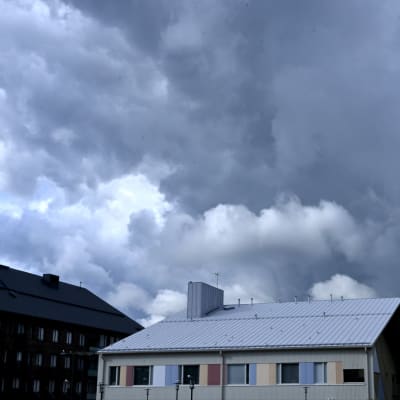 Tummia pilviä taivaalla talon takana.