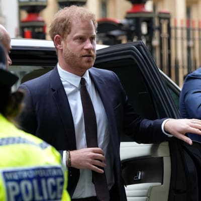 Prins Harry stiger ur en bil. Han är omgiven av säkerhetsvakter och poliser.