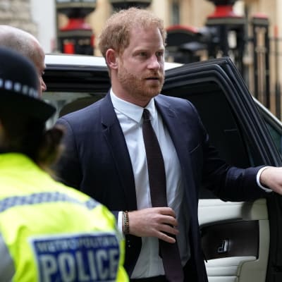 Prins Harry stiger ur en bil. Han är omgiven av säkerhetsvakter och poliser.