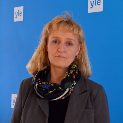 Marianne Pekola-Sjöblom står framför en blåvägg med Yle-logon.