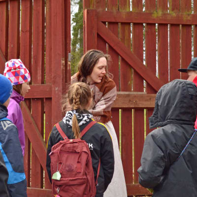 Pigan (Helena Laxén) öppnar en grind för skolbarn som deltar i ett skådespel.