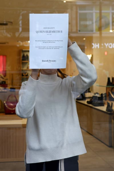 En person tejpar upp ett vitt pappersark med information på en affärsdörr.