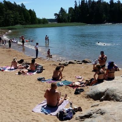 Folk solbadar och simmar vid en simstrand en solig sommardag.