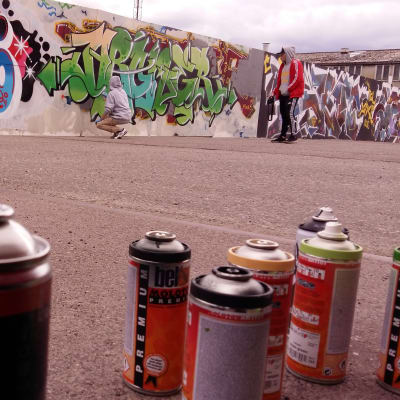 Sprayburkar som en graffitiartist använder på en vägg vid ett bygge.