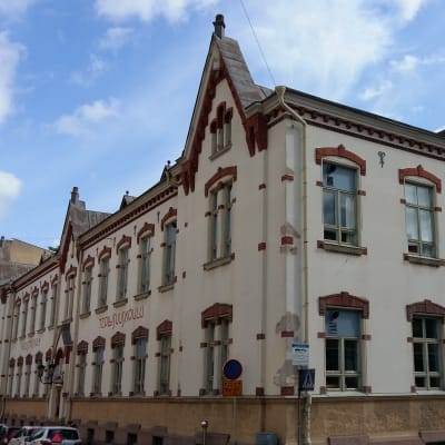 En skola med spetsiga gavlar och vacker tegelstensutsmyckning kring fönstren i ett gathörn i Åbo.
