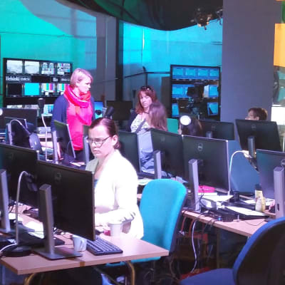 Människor sitter vid datorer i kulisserna till Yles OS-studio.