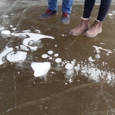 Två par skor står vid bubblor som frusit fast i isen.