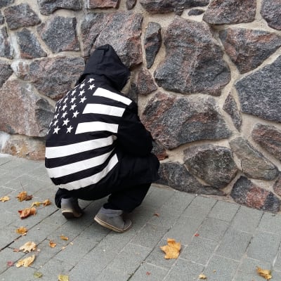Kille med ryggen mot kameran vid stenvägg.