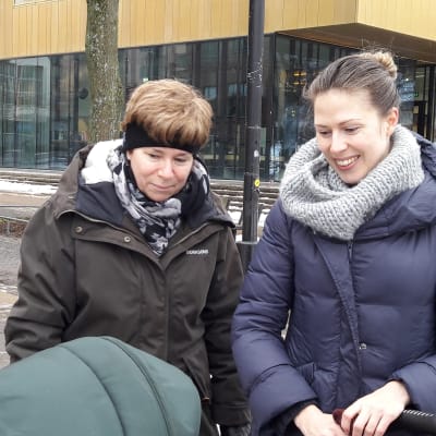Maria Bratt med sin mamma, småler, tittar på barnet i barnvagnen.