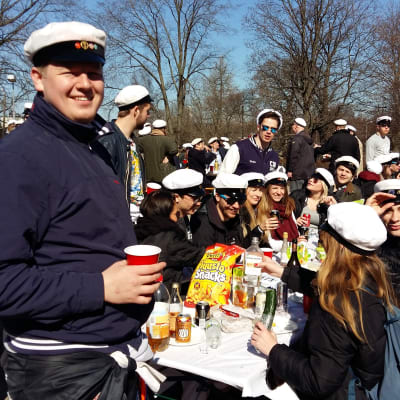 Hankens studentkår SHS har samlats kring ett picknickbord i sina vita studentoveraller.