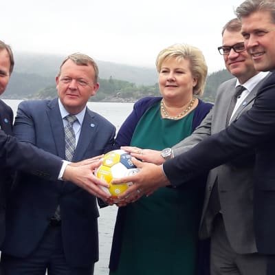 Ministrarna håller handen på en fotboll som har ett globalt hållbarhetsbudskap. Hav och fjäll i bakgrunden.