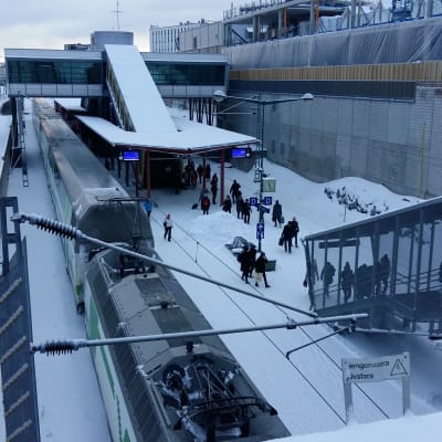 Folk stiger av tåget på en snöig perrong vid Kuppis station.