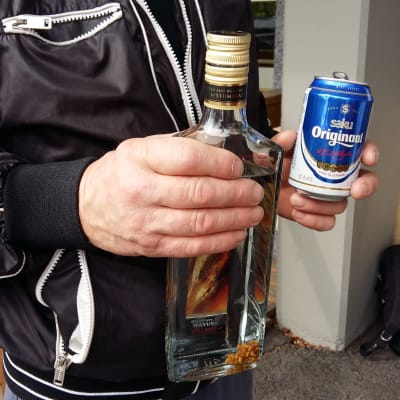En man håller i en flaska starksprit och en burk öl.