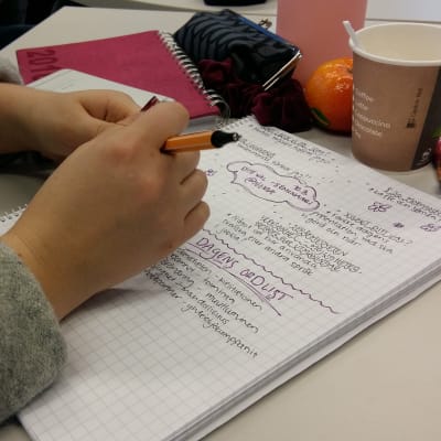 En student gör anteckningar i sitt häfte på två språk.