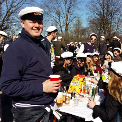 Hankens studentkår SHS har samlats kring ett picknickbord i sina vita studentoveraller.