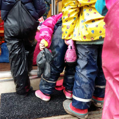 Daghemsbarn i regnkläder köar för att komma in till dagiset.