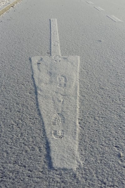 En pil på vägen går åt ena hållet, fotstegen i snön åt det andra hållet.