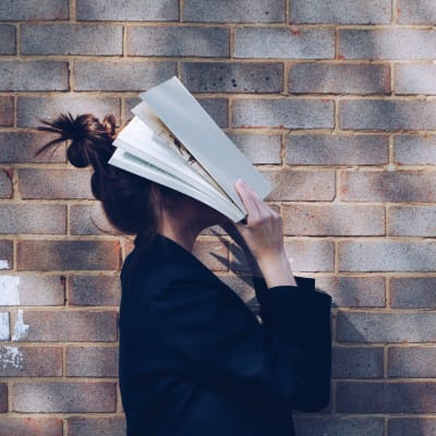 En kvinna täcker sitt ansikte med en bok.