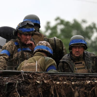 Fyra ukrainska soldater står i ett militärfordon. Det är grått och regnigt väder.