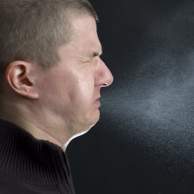 En man nyser och det sprutar ut partiklar ur hans mun.