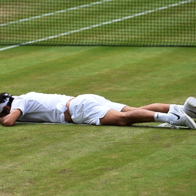 Roger Federer ligger utmattad på planen i Wimbledon-semifinalen mot Milos Raonic.