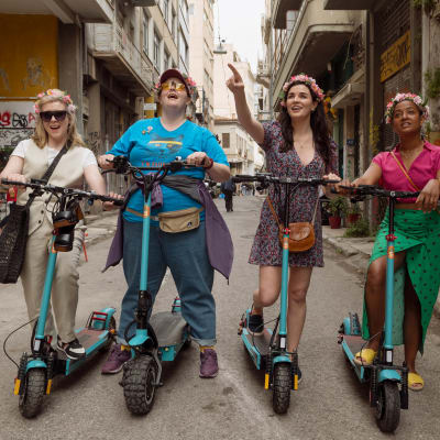 Fyra kvinnor står bredvid varandra på en mindre gata. De håller alla i varsin elsparkcykel.