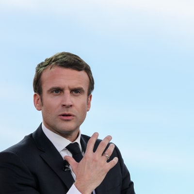 Emmanuel Macron gestikulerar med blå himmel i bakgrunden.