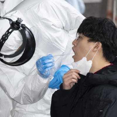 Hälsovårdsarbetare i skyddsutrustning tar covid-19-prov ur munnen på en person. Fotograferat i Seoul i mars 2020.