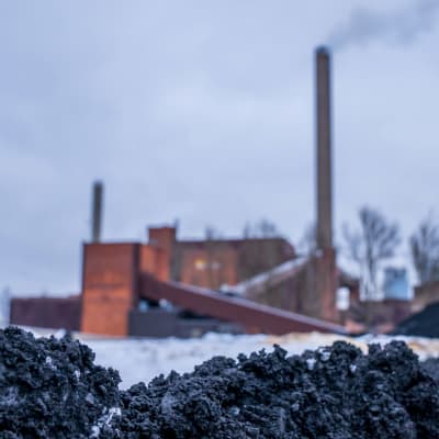 Kolkraftverket på Hanaholmen i Helsingfors fotograferat på mrknivå med svart lera eller kol i förgrunden. 