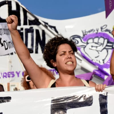 En kvinna håller i en skylt och håller upp en hand medan hon demonstrerar.