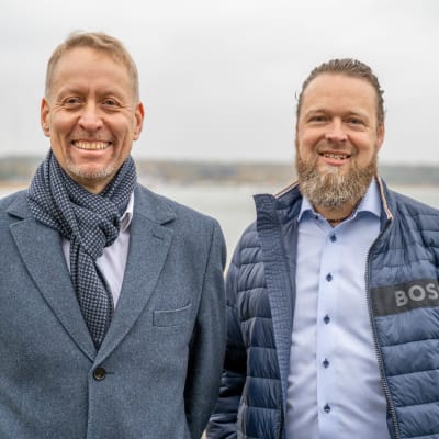 Två män i närbild. I bakgrunden havet.