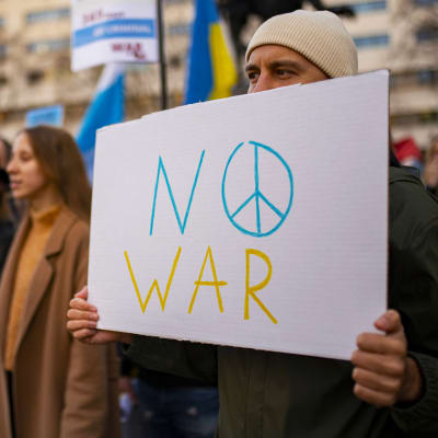 En man håller i en skylt med texten "No war" i gult och blått under en demonstration i Barcelona den 25 februari 2023.