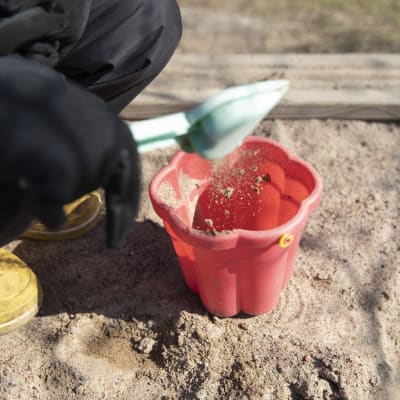 Ett barn häller sand i en hink i sandlådan.