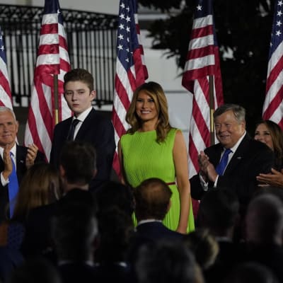 Barron Trump bredvid sin mamma Melania Trump. I bakgrunden applåderande politiker.