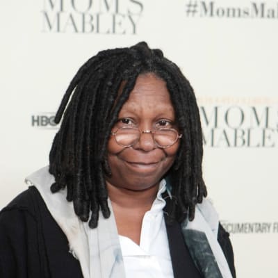 Whoopi Goldberg tittar in i kameran. Hon är fotograferad framför en vit vägg.