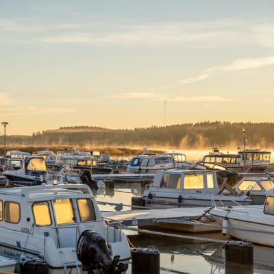 Båtar vid en båthamn en höstmorgon, på havet syns lite dimma som stiger upp.