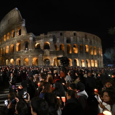 Ihmiset kantavat soihtuja ja kynttilöitä Rooman Colosseumin edessä.