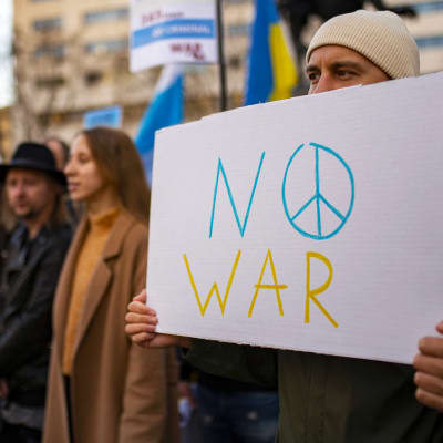 En man håller i en skylt med texten "No war" i gult och blått under en demonstration i Barcelona den 25 februari 2023.