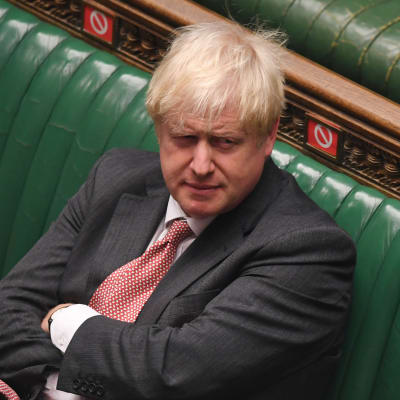 Boris Johnson sitter ensam med korslagda armar på en av de gröna bänkarna i parlamentet. 