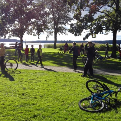 En park där det går och cyklar flera barn som spelar Pokémon Go.