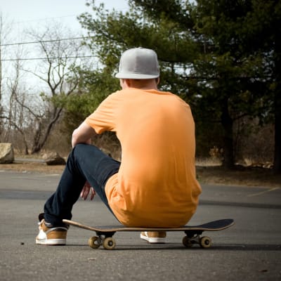 En pojke sitter på en skateboard med ryggen mot kameran.