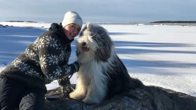Patrica Strömbäck med sin hund på en sten vid en frusen strand.