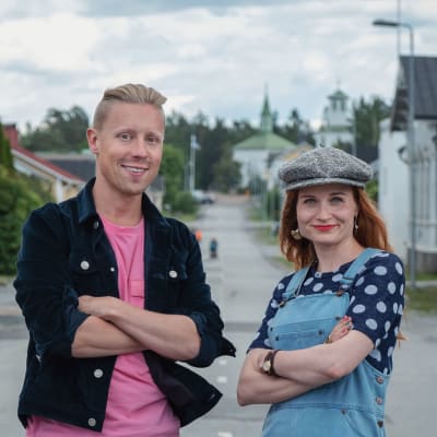 Egenland-ohjelman juontajat Nicke Aldén ja Hannamari Hoikkala seisovat keskellä katua Porin Reposaaressa, sivuilla näkyy puutaloja. 